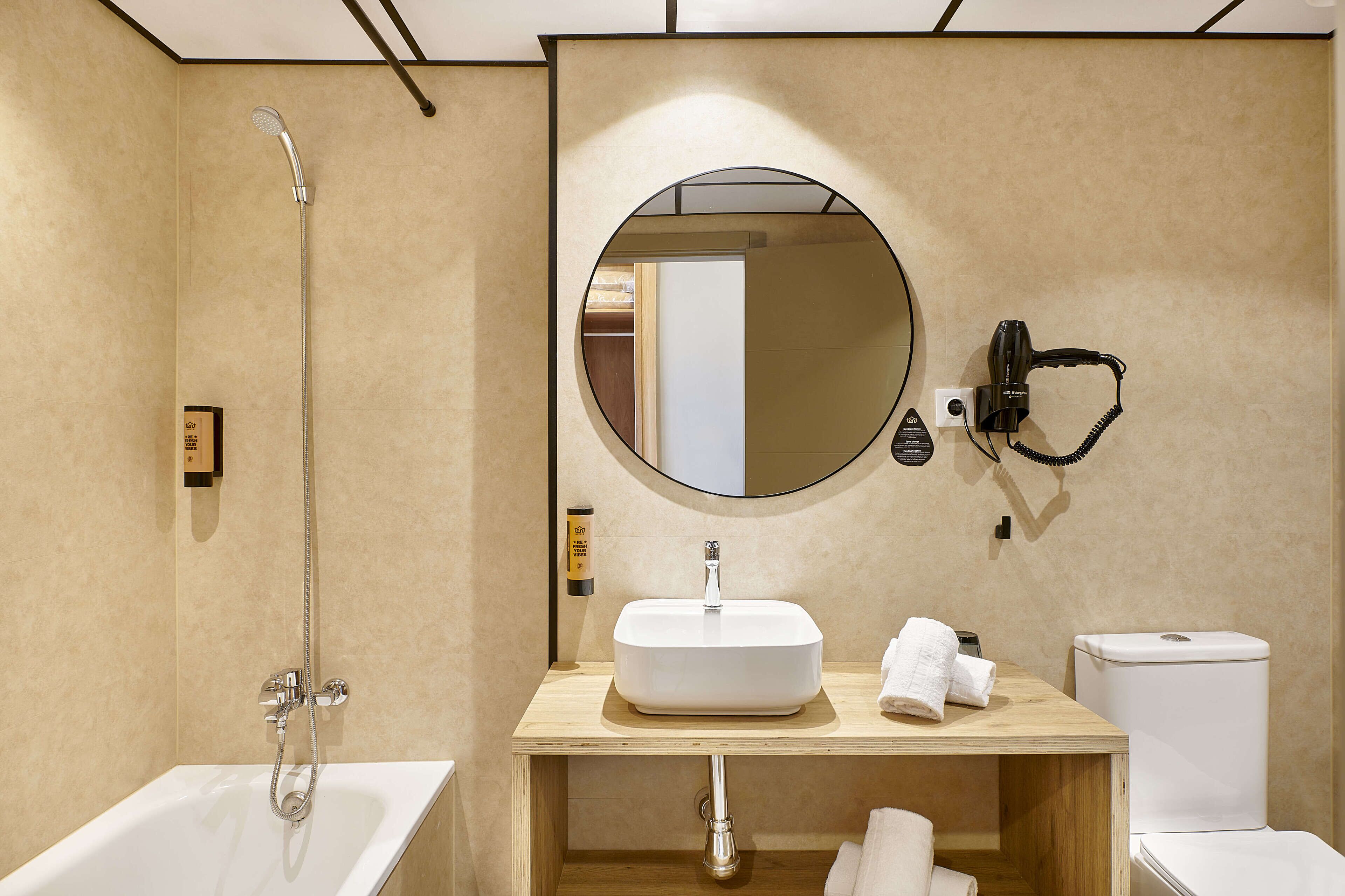 A modern bathroom with a freestanding bathtub, a round mirror, a handheld hair dryer, and a toilet.