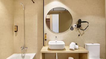 A modern bathroom with a freestanding bathtub, a round mirror, a handheld hair dryer, and a toilet.