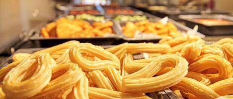 Un bufé con diversos alimentos, entre ellos churros y otras opciones de repostería.