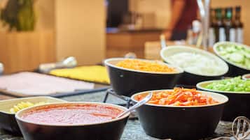 Una mesa de buffet con diversos platos, incluyendo pasta, verduras y salsa roja.