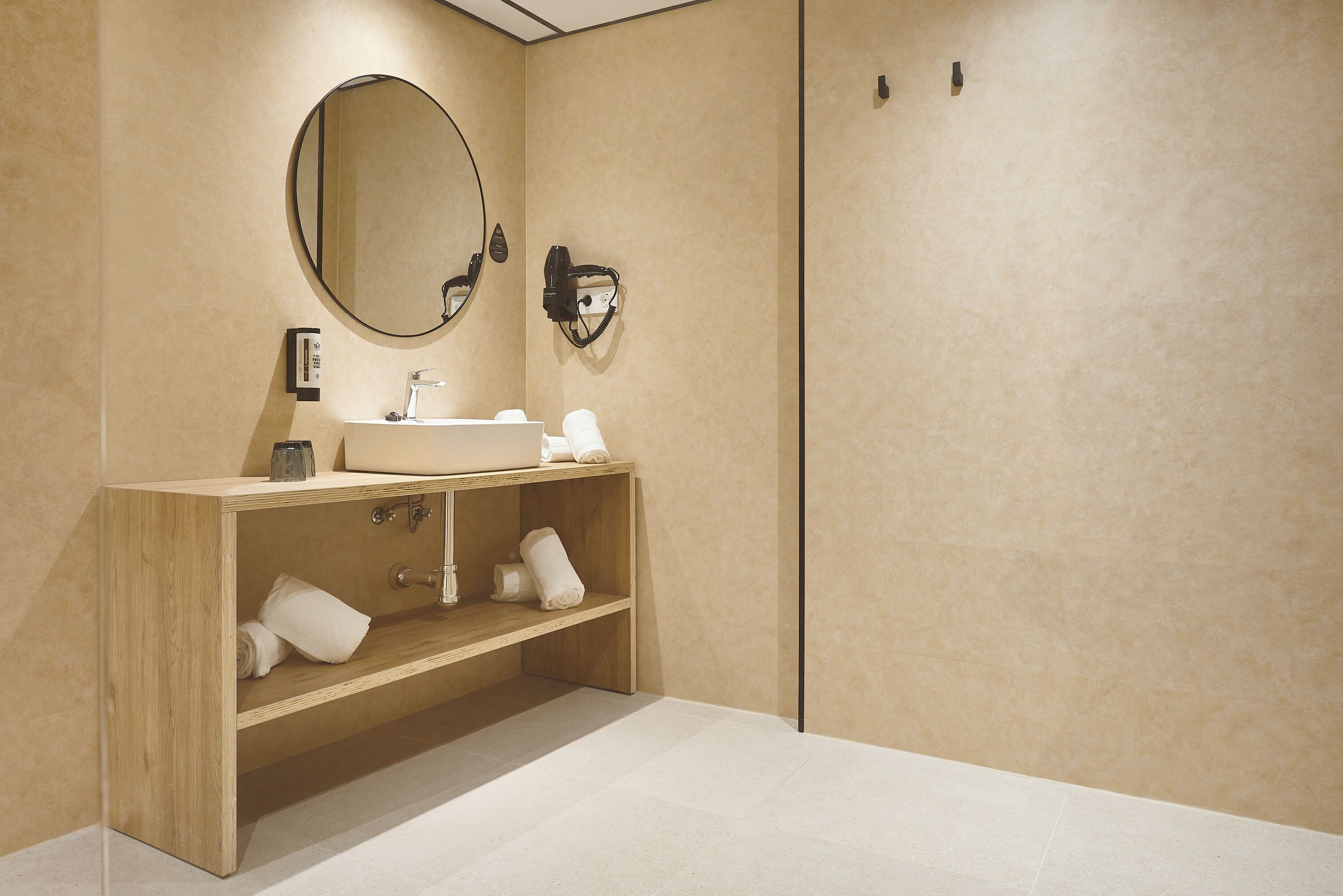 Een moderne badkamer met een houten wastafelmeubel, een ronde spiegel en een handdoekrek.