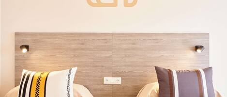 Habitación de hotel con cabecera de madera, dos mesitas de noche y dos almohadas con estampados a rayas.