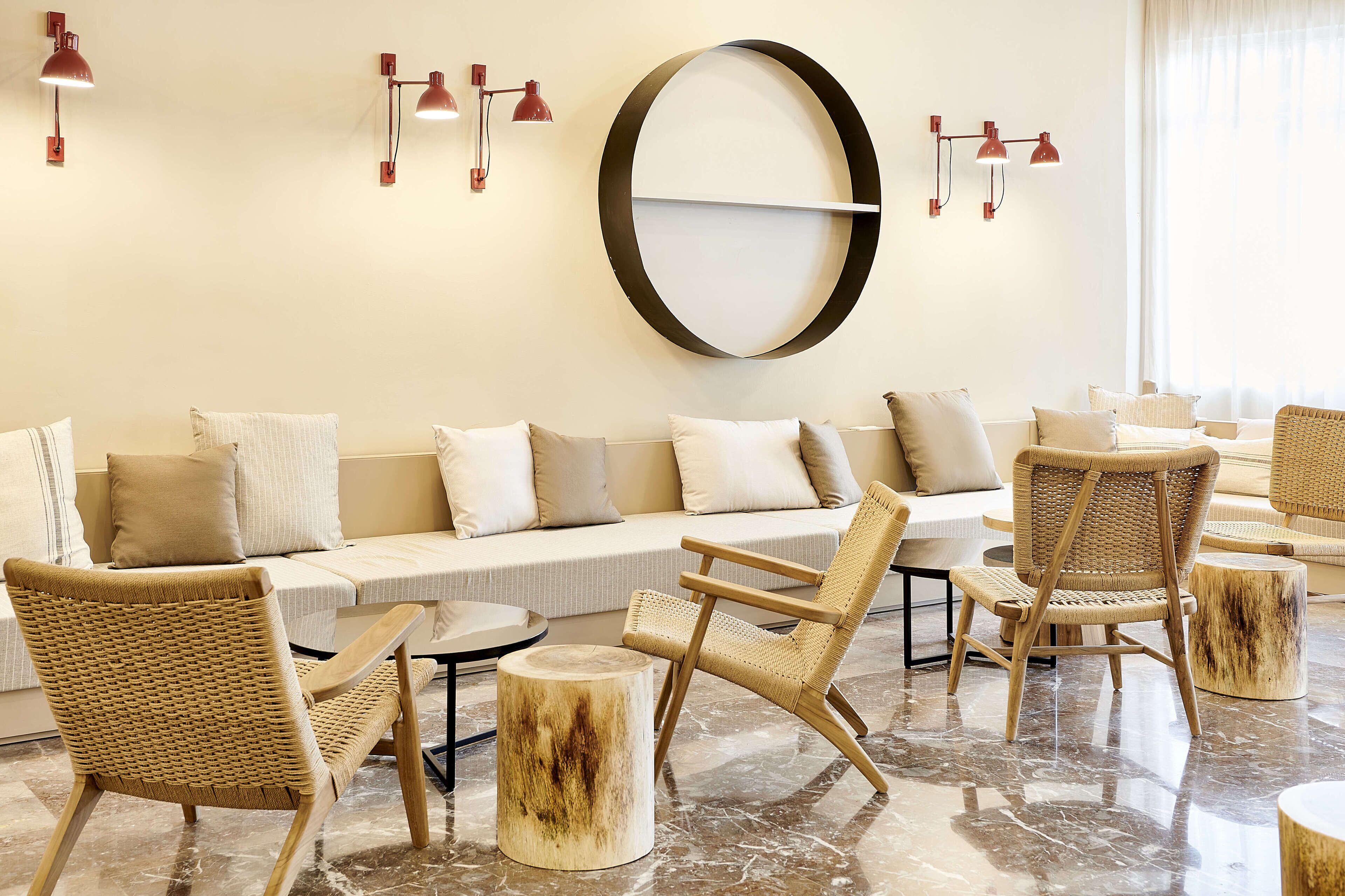 A modern lounge area with a sofa, wicker chairs, and a round mirror on the wall.