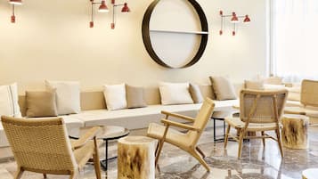 Un espace de détente moderne avec un canapé, des fauteuils en osier et un grand miroir rond accroché au mur.