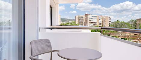 A balcony with a chair and table, overlooking a cityscape with buildings and greenery.