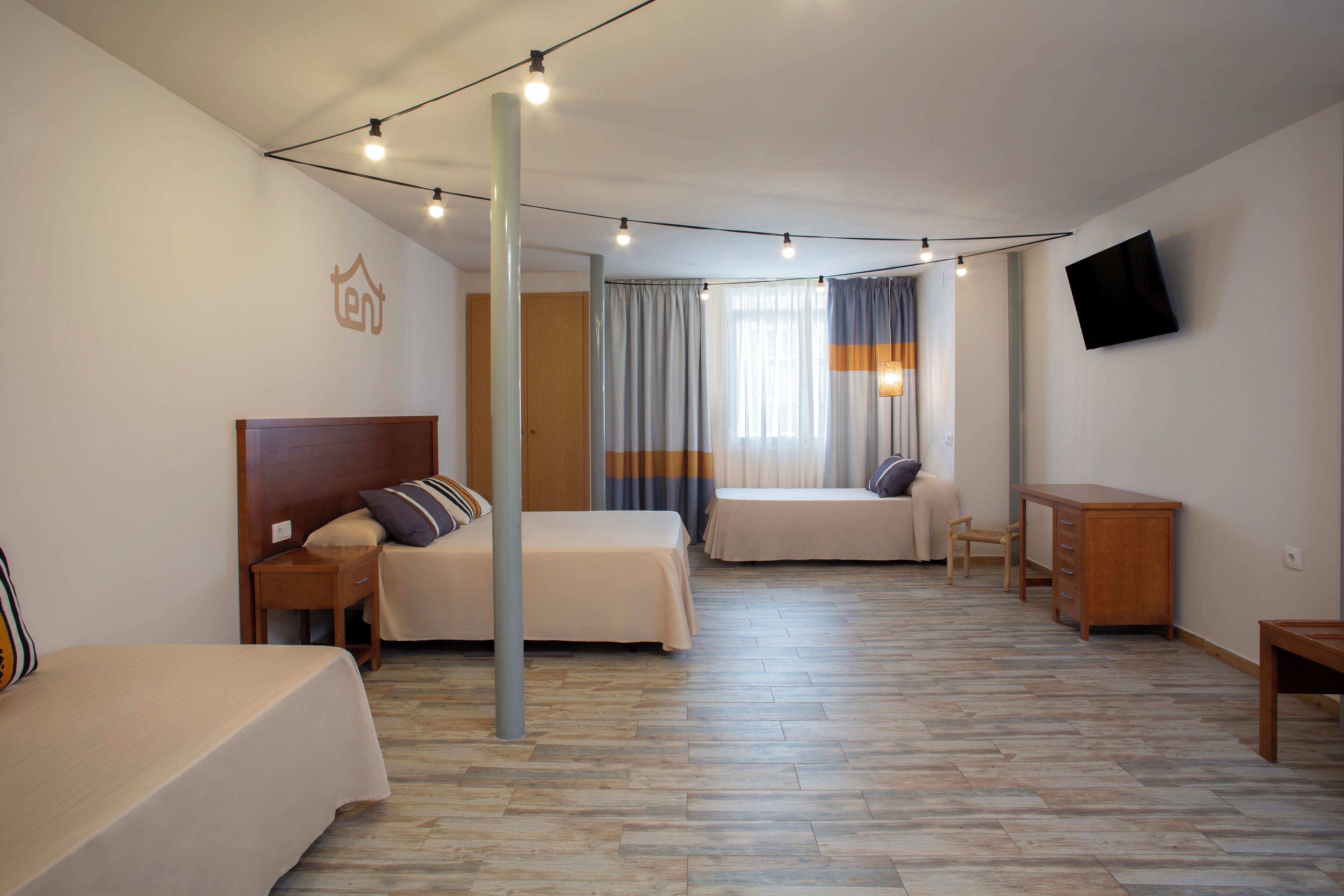 A hotel room with two beds, a desk, a chair, a TV, and a window with curtains.