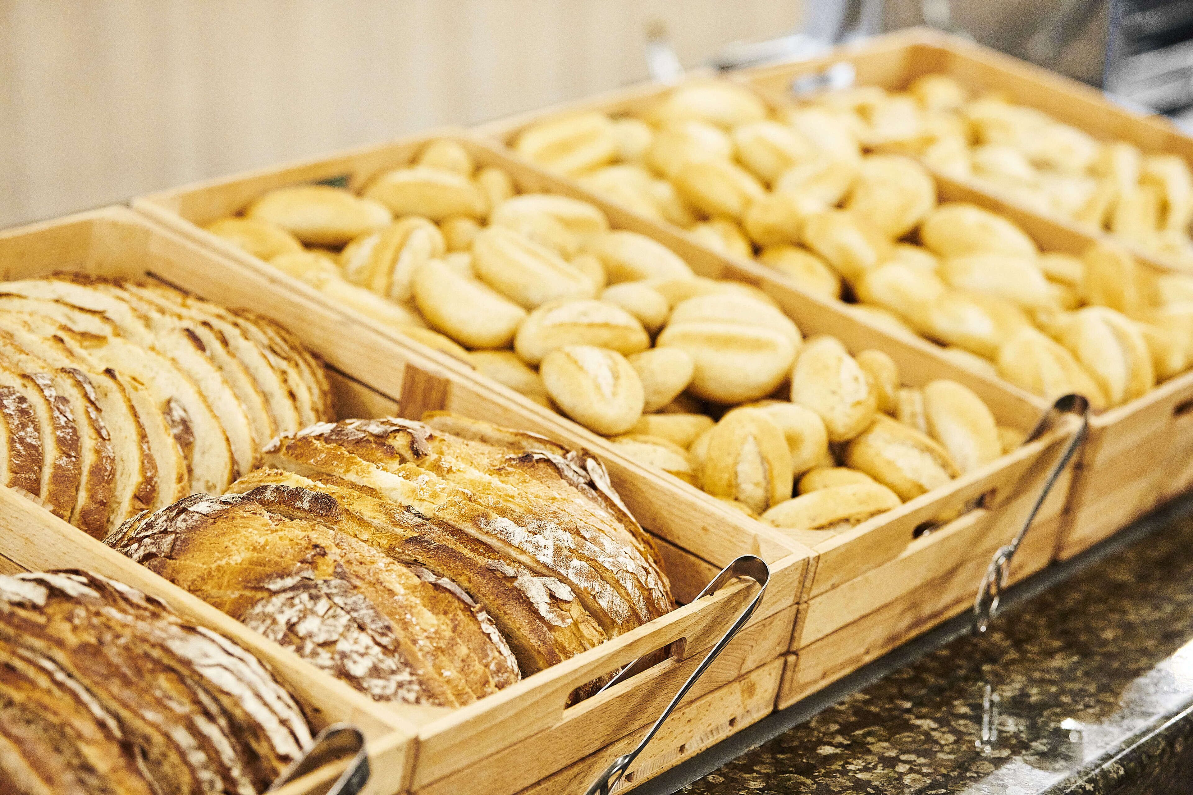 Une variété de pains et de viennoiseries présentés dans des plateaux en bois.