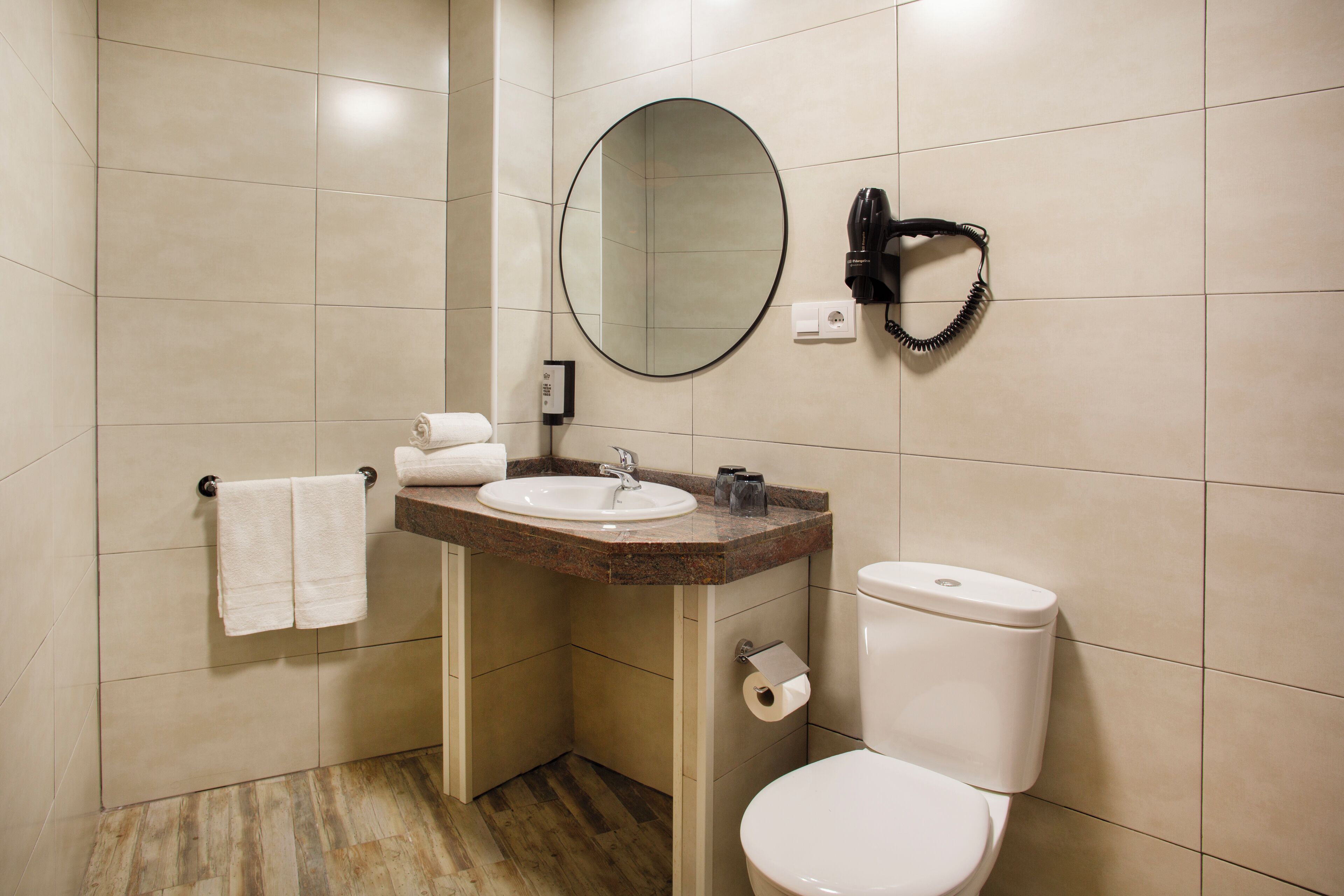 Un baño con lavamanos, espejo, toallero, inodoro y secador de pelo.