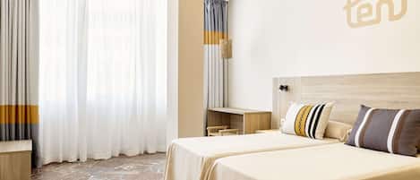 A hotel room with two beds, a desk, and a large window with curtains.