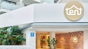 Une entrée d’hôtel moderne avec un logo représentant le chiffre « 10 », un panneau indiquant un espace de jeux et un mur en briques.