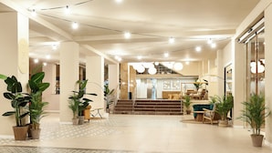Un hall d’entrée spacieux, doté d’un sol à motifs, de plantes en pot, d’un escalier et d’un coin salon avec un canapé et des fauteuils.