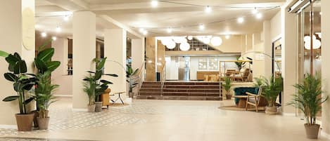 A spacious lobby with a patterned floor, potted plants, a staircase, and a seating area with a sofa and chairs.
