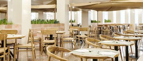 A restaurant with wooden chairs and tables, large windows, and indoor plants.