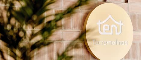 A circular sign with a house icon and the text "Torremolinos" on a brick wall.