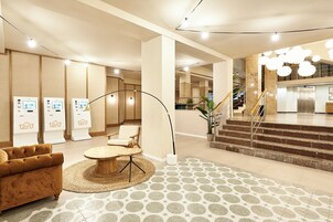 A modern lobby with a sofa, a round table, a staircase, and a reception desk.