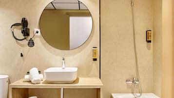Un baño moderno con un espejo redondo, un lavabo blanco, un secador de pelo portátil, un cabezal de ducha manual y una bañera.