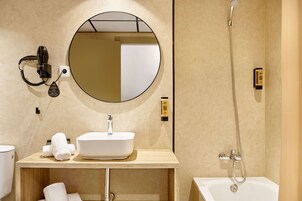 Un baño moderno con un espejo redondo, un lavabo blanco, un secador de pelo portátil, un cabezal de ducha manual y una bañera.
