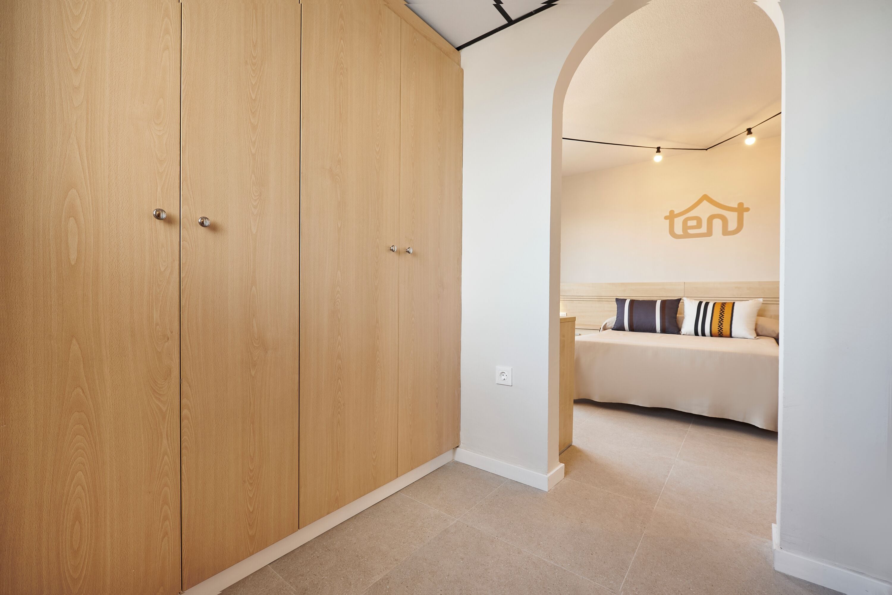 A spacious room with a large wooden wardrobe, a cozy sofa with patterned cushions, and a minimalist design.