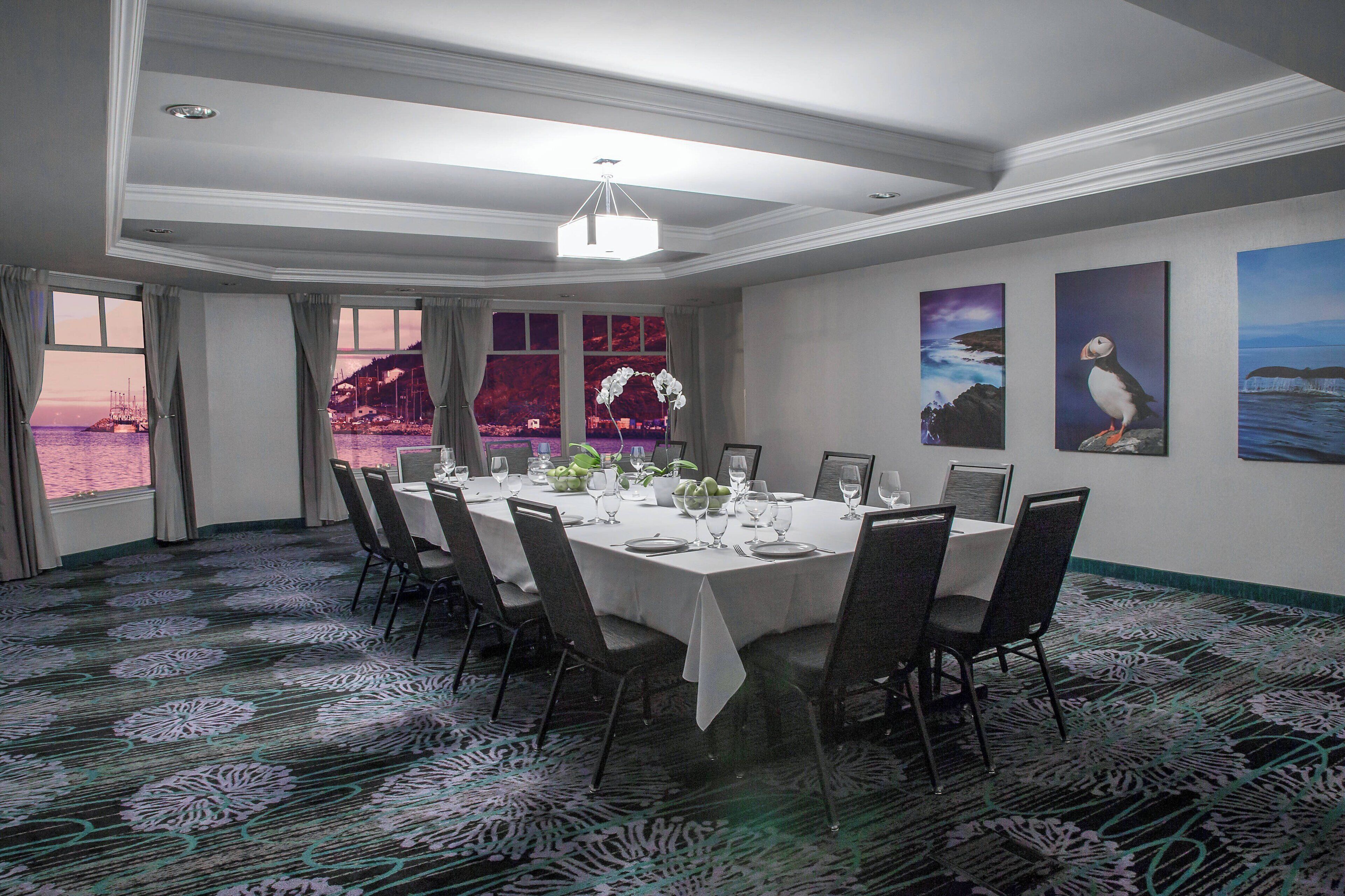 A conference room with a round table, chairs, and a view of the sea through large windows.