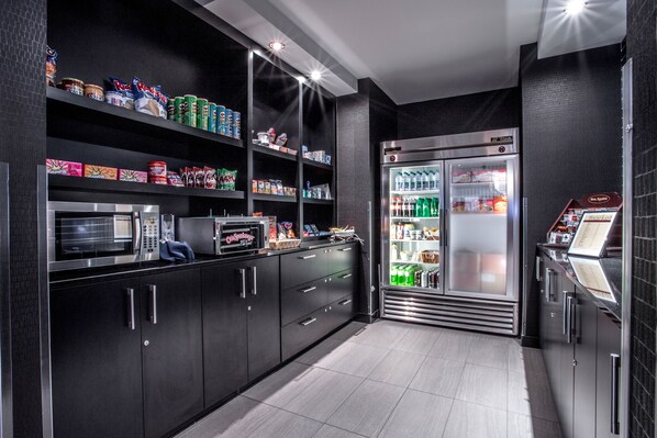 A modern kitchen with black cabinets, stainless steel appliances, and a refrigerator stocked with beverages.