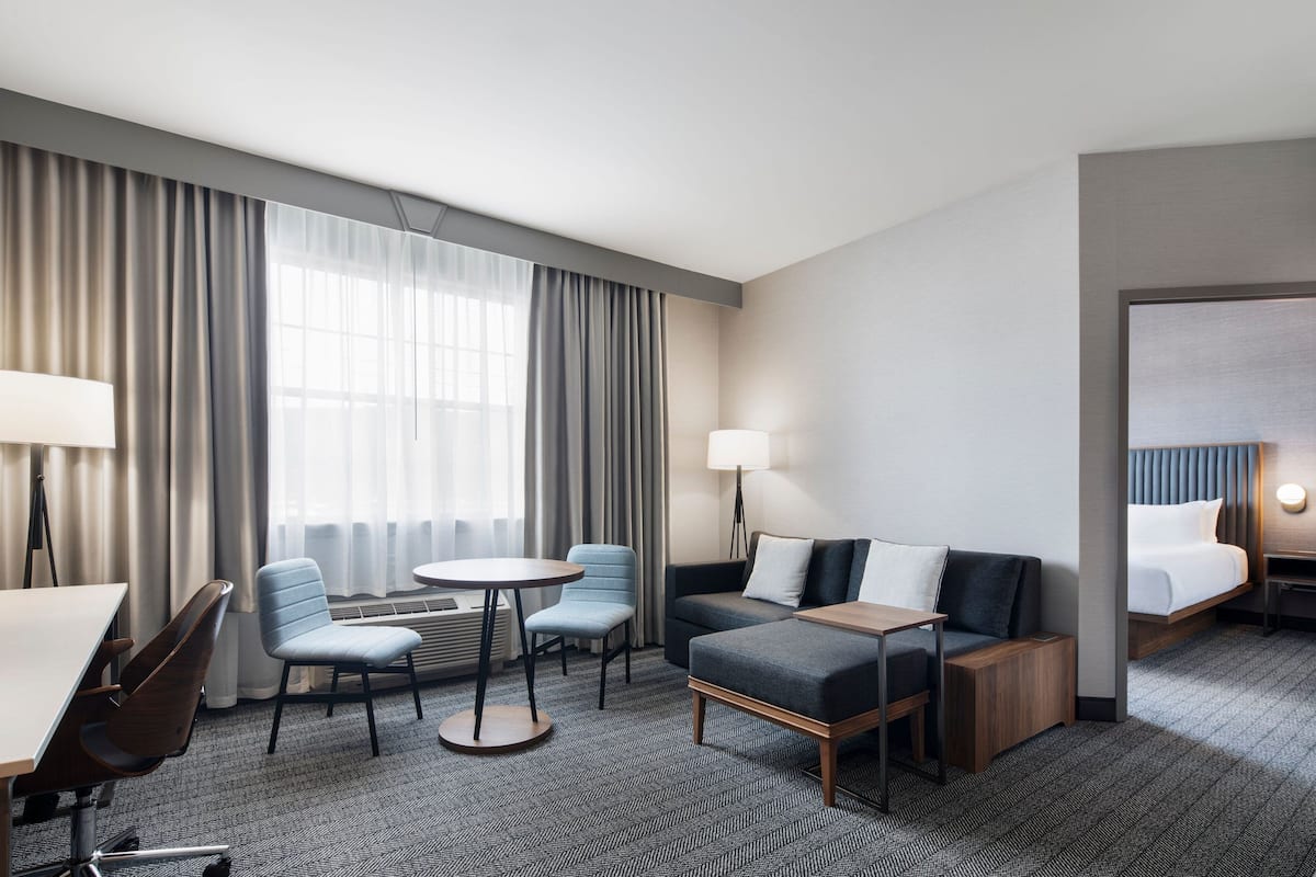 A hotel room with a bed, a sofa, a desk, a chair, and a small table.