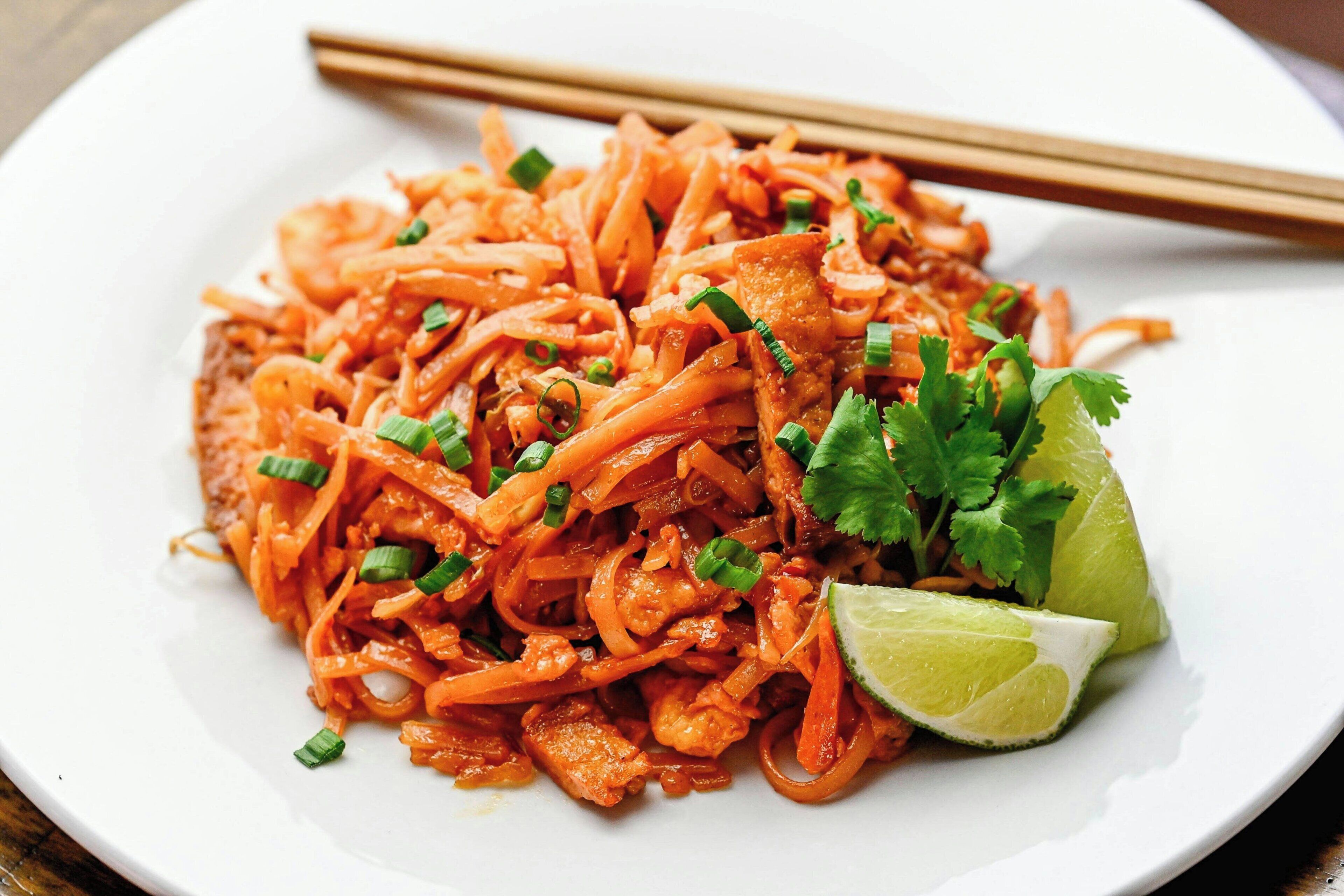 Un plato de fideos salteados con zanahorias, aderezado con cilantro y una cuña de lima.