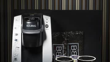 Una cafetera Keurig con dos tazas de café negro y un paquete de cápsulas de café sobre una superficie reflectante.