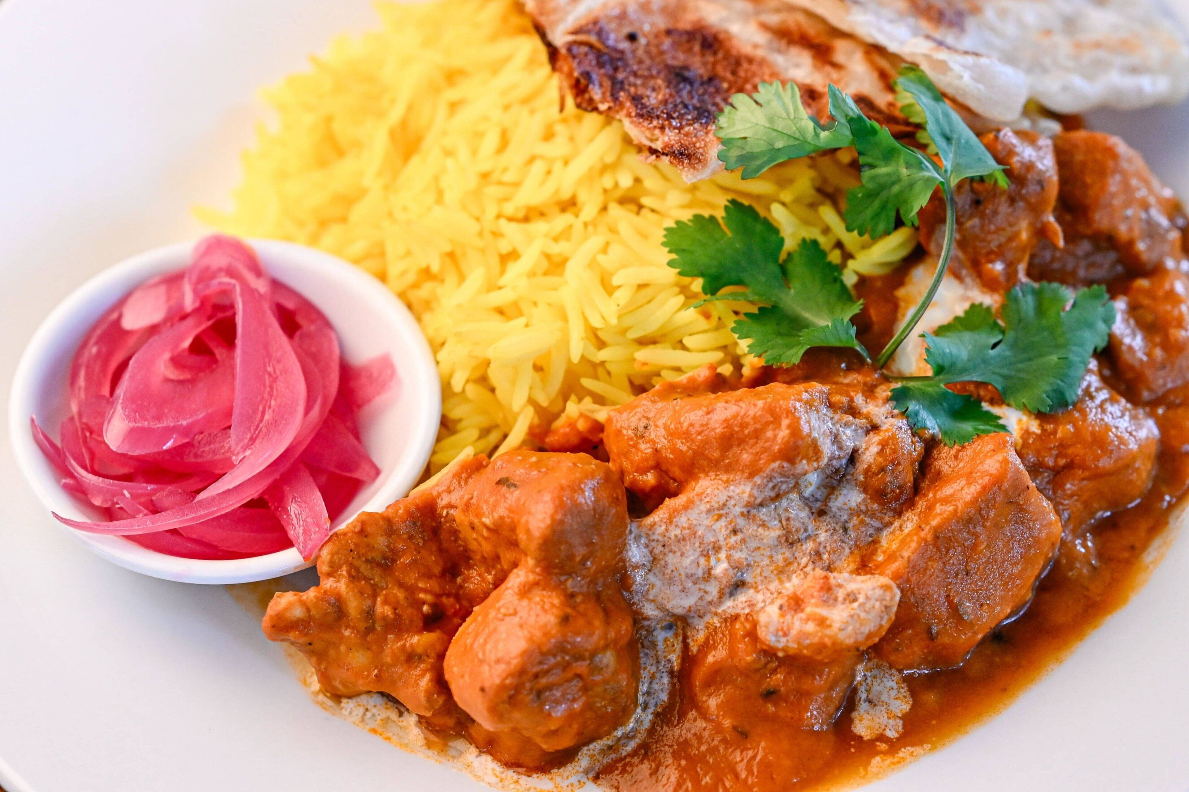 Un plato de comida con arroz amarillo, un guiso de carne y cebollas encurtidas.