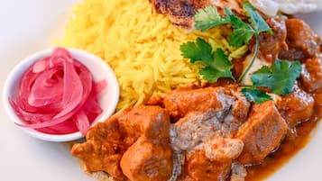Un plato de comida con arroz amarillo, un guiso de carne y cebollas encurtidas.