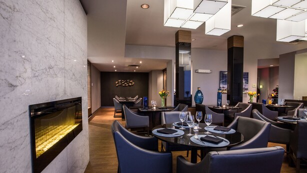 A modern dining area with marble walls, black leather chairs, and a central fireplace. - Courtyard by Marriott St. John's Newfoundland (St. John's)