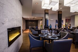 A modern dining area with marble walls, black leather chairs, and a central fireplace.