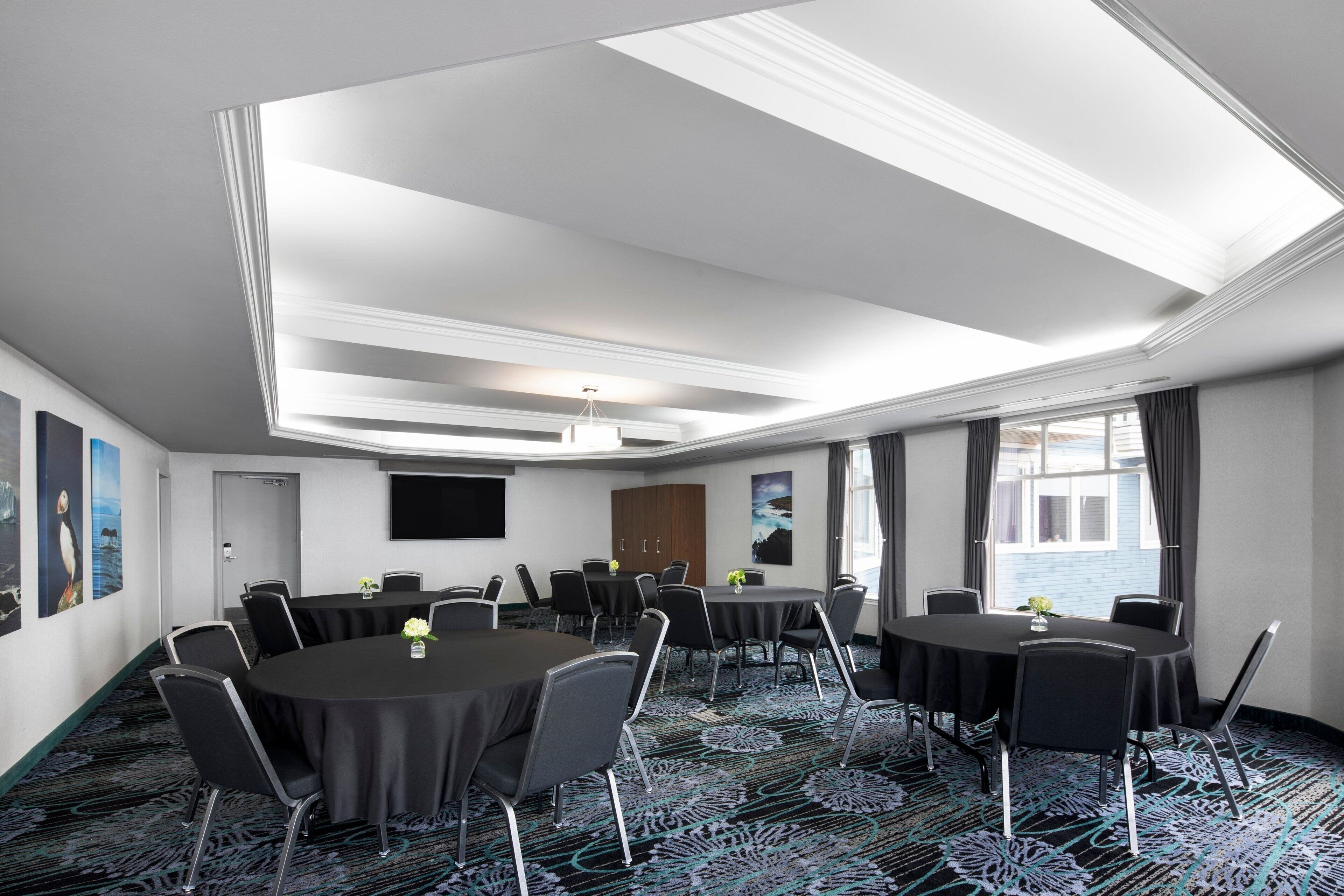 Une salle de conférence équipée de tables rondes, de chaises, d’un téléviseur à écran plat et ornée d’œuvres d’art sur les murs.