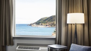 A room with a large window overlooking a coastal view, a standing lamp, and an air conditioning unit. - Courtyard by Marriott St. John's Newfoundland (St. John's)