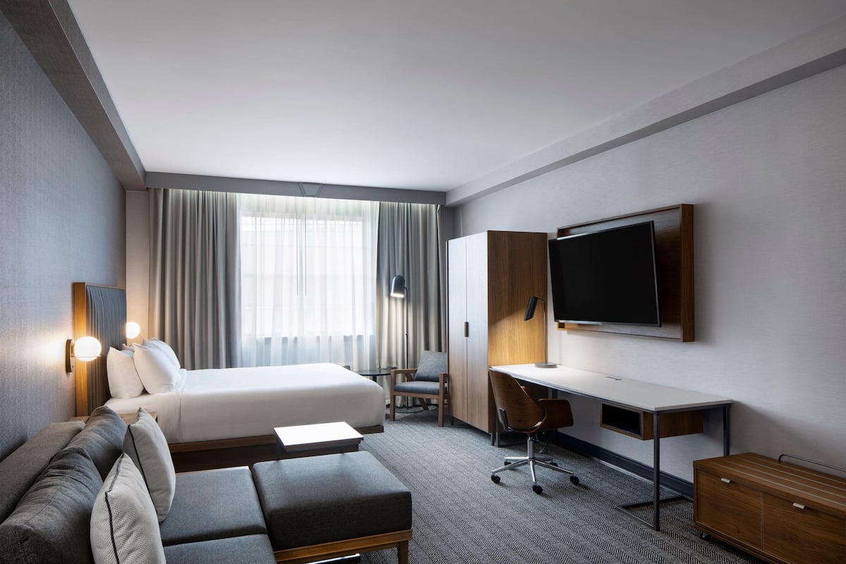 A hotel room with a bed, a desk, a chair, and a TV.