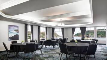 A conference room with round tables and chairs, large windows with curtains, and a view of a landscape.