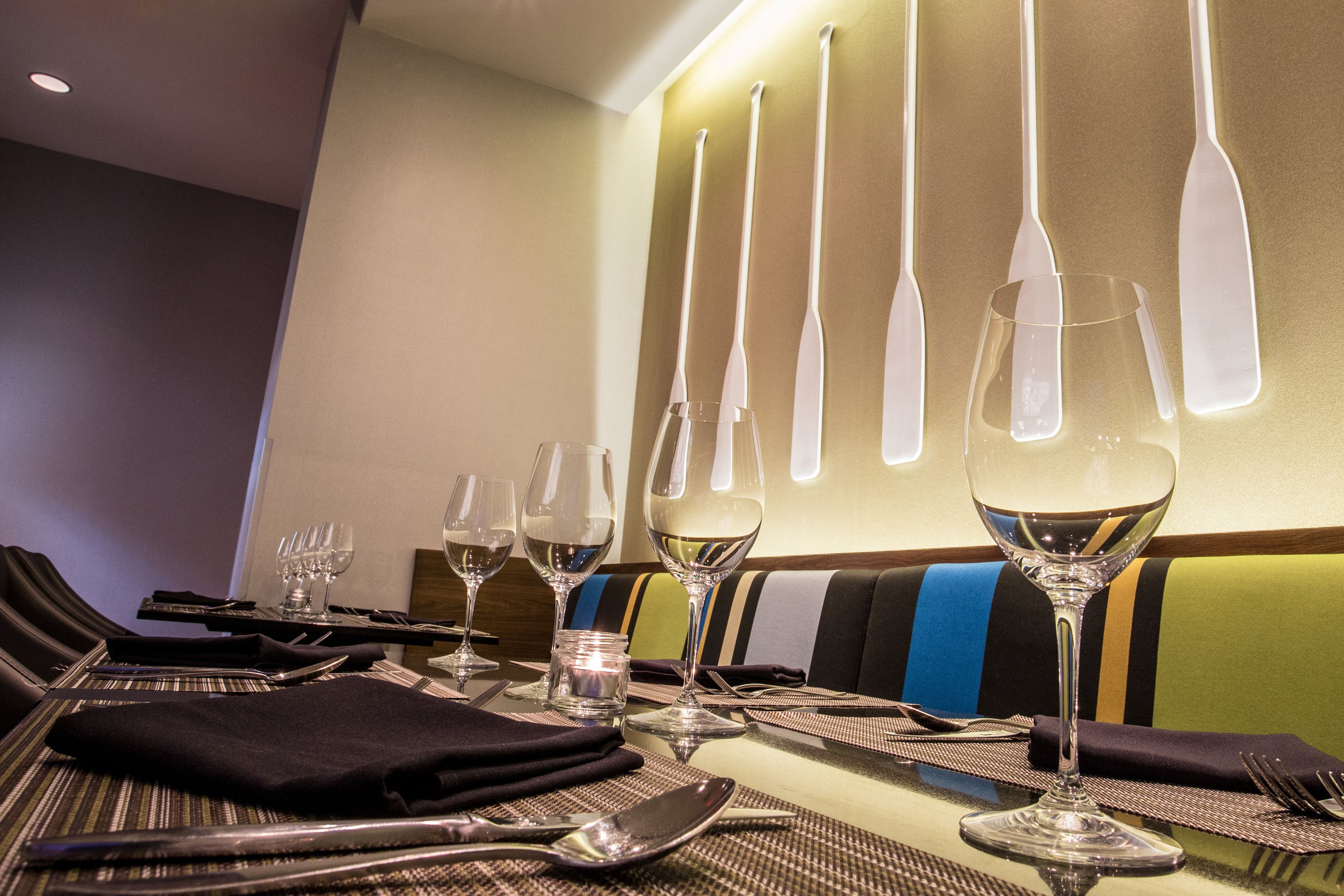 Une table à manger dressée avec des verres à vin, des couverts et des sets de table.