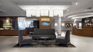 A modern hotel lobby with a reception desk, a seating area with a round table, and a large painting on the wall. - Courtyard by Marriott St. John's Newfoundland (St. John's)