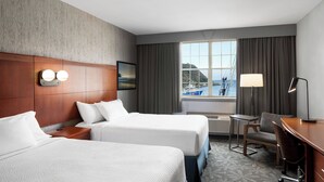 A hotel room with two beds, a desk, a chair, a lamp, a view of the sea, and a window with curtains. - Courtyard by Marriott St. John's Newfoundland (St. John's)