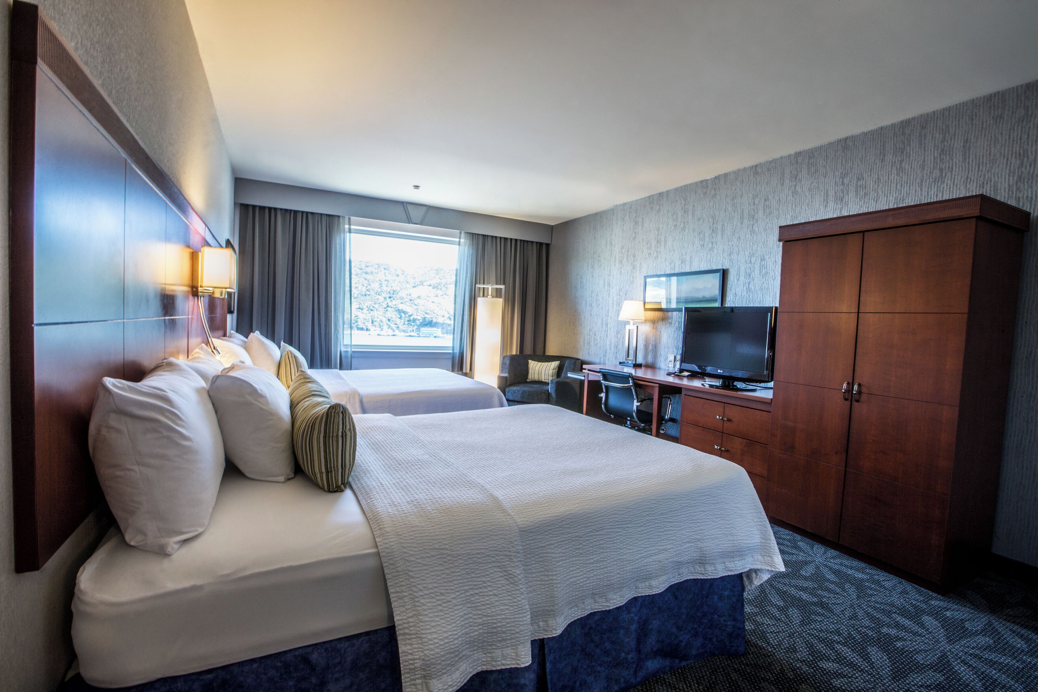 A hotel room with a large bed, a desk with a computer, a TV, and a wardrobe.