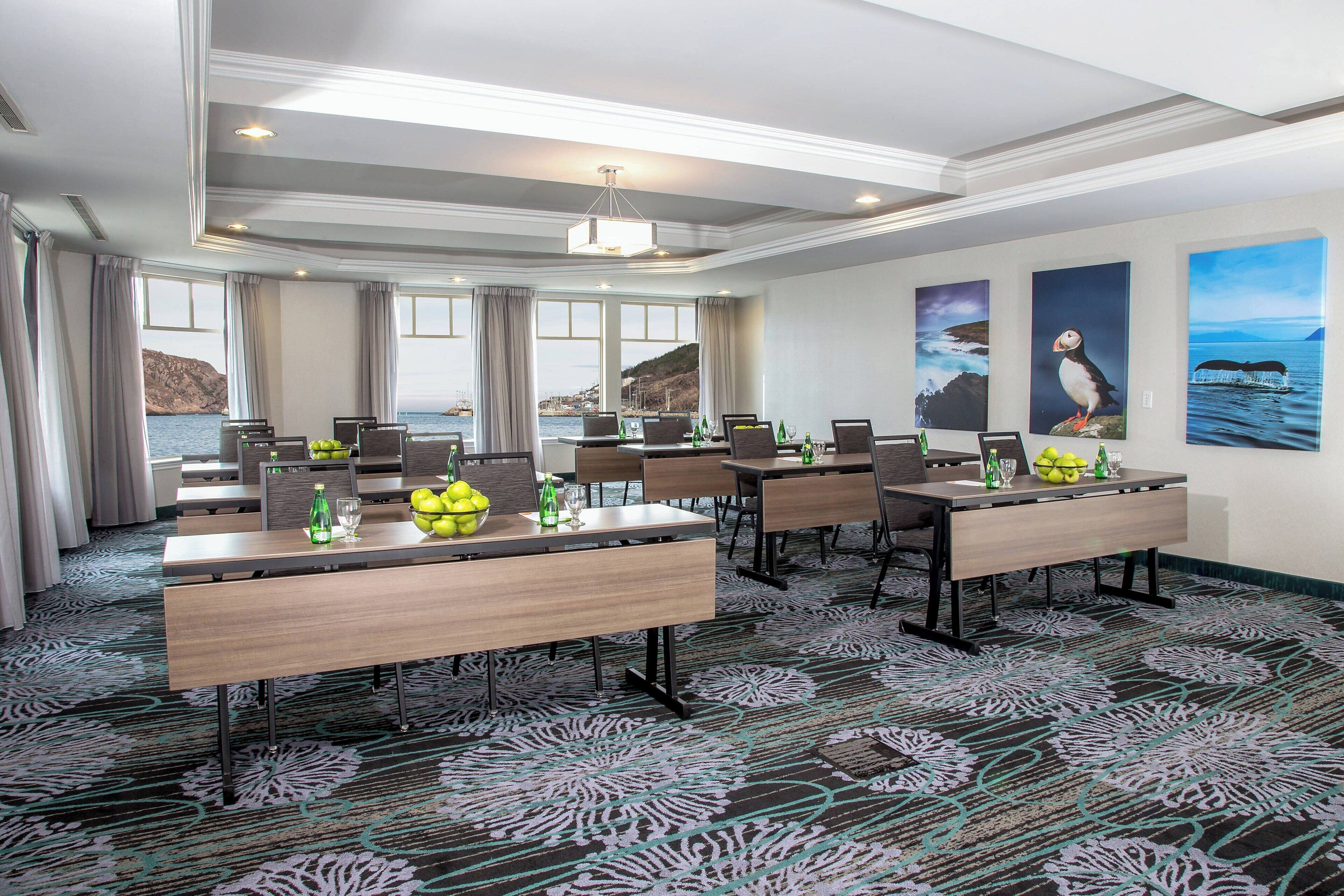 A conference room with multiple tables, chairs, and laptops, featuring a coastal view through large windows.