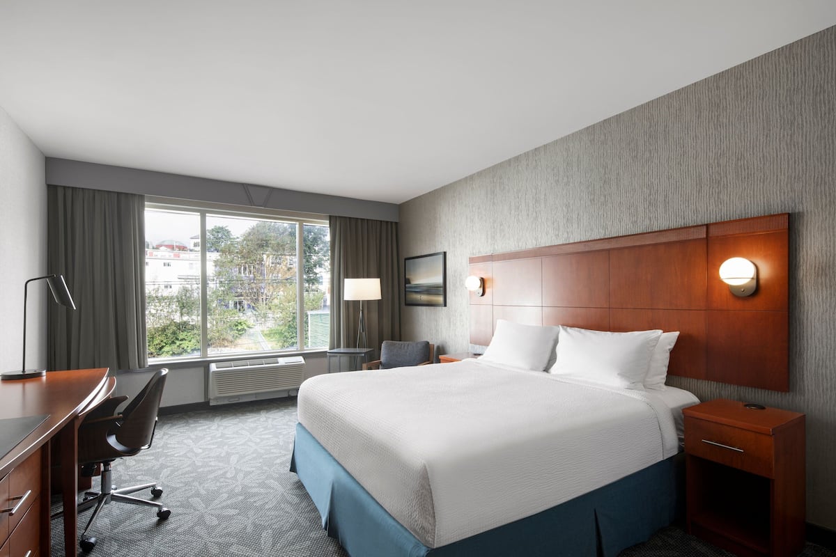A hotel room with a large bed, a desk, a chair, a nightstand, and a window with curtains.
