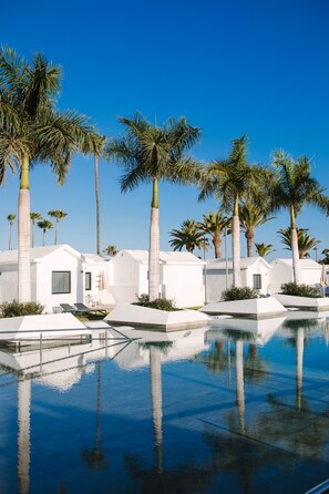 A poolside area with white buildings, palm trees, and clear blue sky. - Club Maspalomas Suites & Spa - Adults Only (San Bartolomé de Tirajana)
