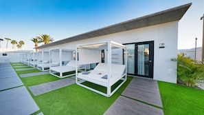 A modern outdoor lounge area with white lounge beds and artificial grass, a concrete roof, and a door with a number sign. - Club Maspalomas Suites & Spa - Adults Only (San Bartolomé de Tirajana)