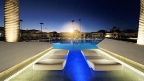 A swimming pool with a water feature, lounge chairs, and palm trees at dusk. - Club Maspalomas Suites & Spa - Adults Only (San Bartolomé de Tirajana)