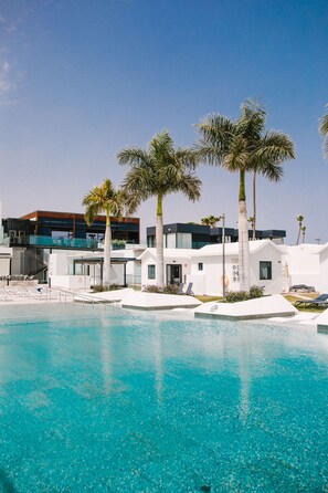 A pool area with clear blue water, palm trees, and modern white buildings in the background. - Club Maspalomas Suites & Spa - Adults Only (San Bartolomé de Tirajana)