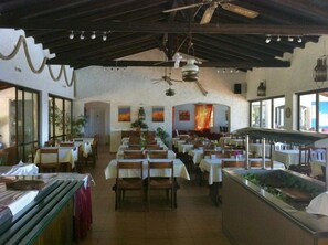 Un restaurante con varias mesas y sillas, un ventilador de techo y obras de arte en las paredes.