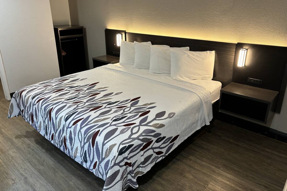 A hotel room with a large bed, a nightstand, a lamp, and a wardrobe.