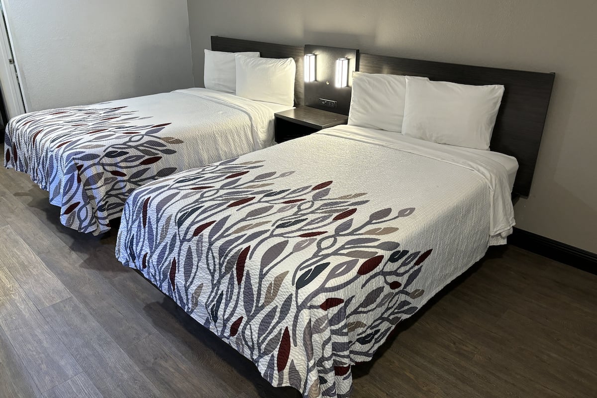 A hotel room with two beds, each with a patterned bedspread, a nightstand with a lamp, and a wooden floor.