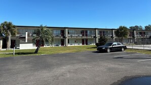 A motel with a two-story structure, featuring a parking lot and a black car parked in the foreground. - Red Roof Inn Wildwood, FL - The Villages (Wildwood)