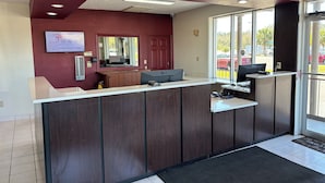 A reception desk with a computer, a mirror, and a window with a view of parked cars outside. - Red Roof Inn Wildwood, FL - The Villages (Wildwood)